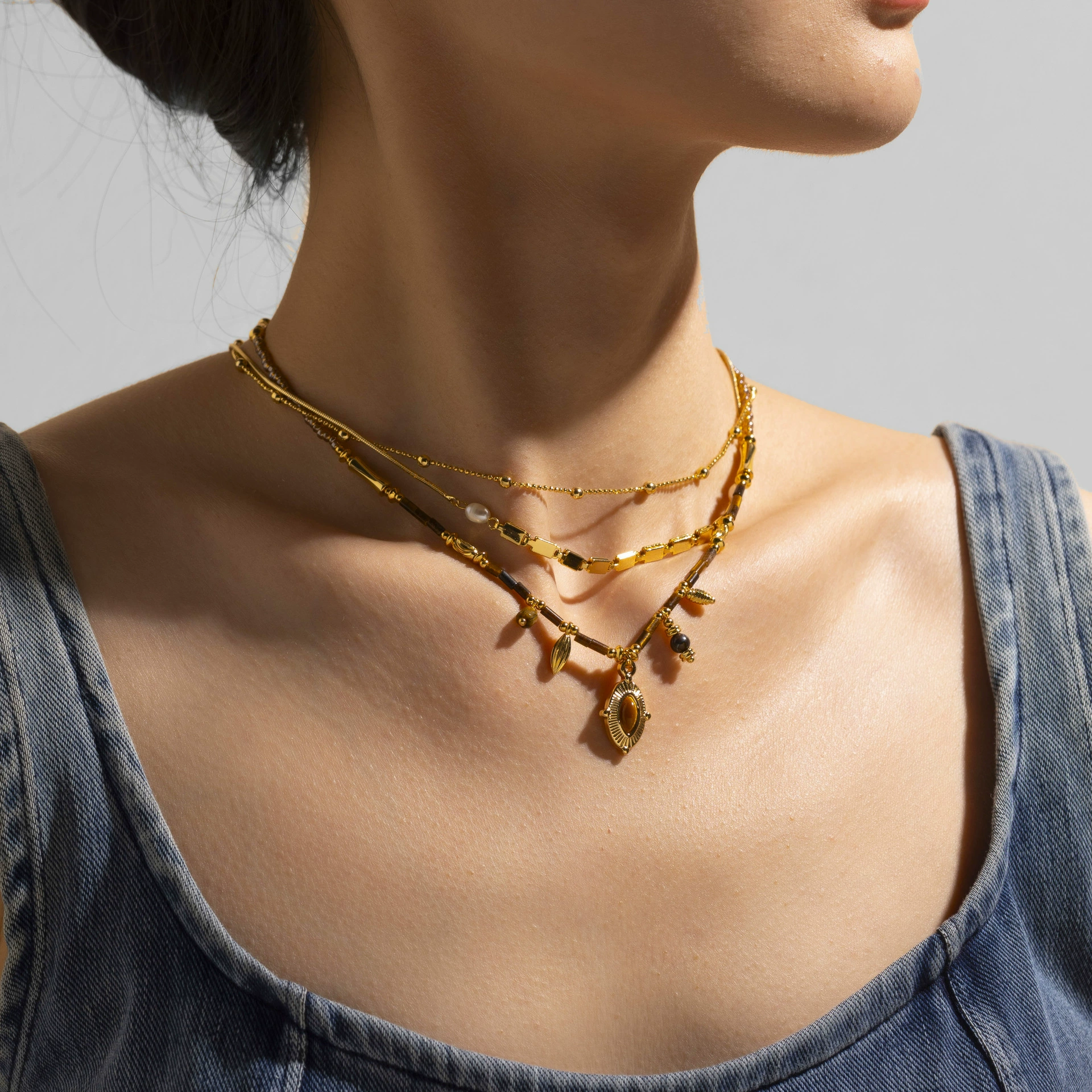 LIVKE’s oval tiger eye necklace with 18K gold-plated chain, styled with black sweater for minimalist elegance.