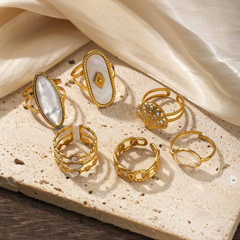 Tanned hand wearing LIVKE shell ring layered with thin gold bands against ocean waves