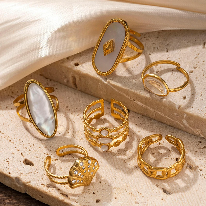 Tanned hand wearing LIVKE shell ring layered with thin gold bands against ocean waves