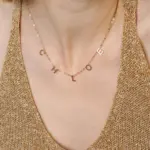 Gold alphabet necklace layered with 4 initials 'LIVK' on collarbone