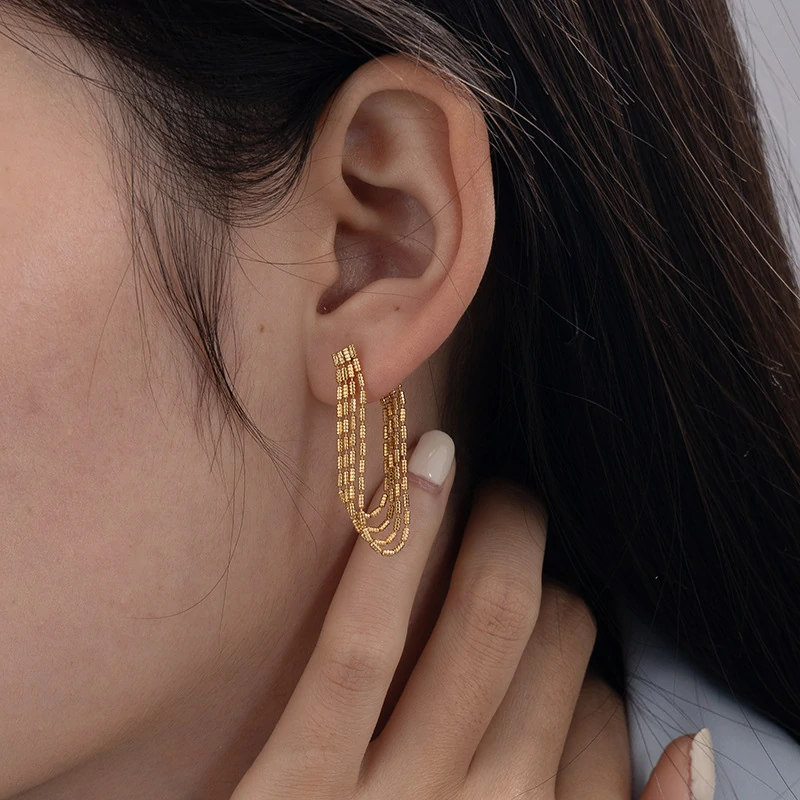Model tilting head to showcase gold chain drops catching sunlight