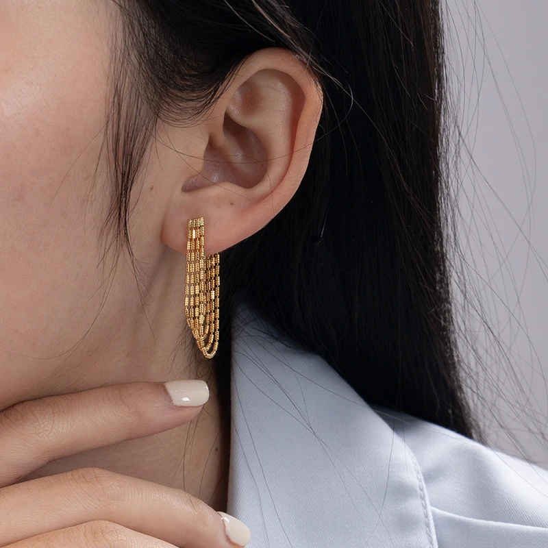 Model tilting head to showcase gold chain drops catching sunlight