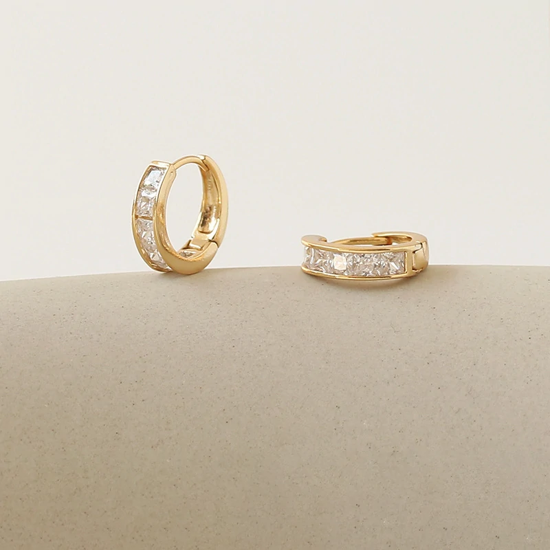Gold ear cuff with square CZ stones on model's ear catching sunlight