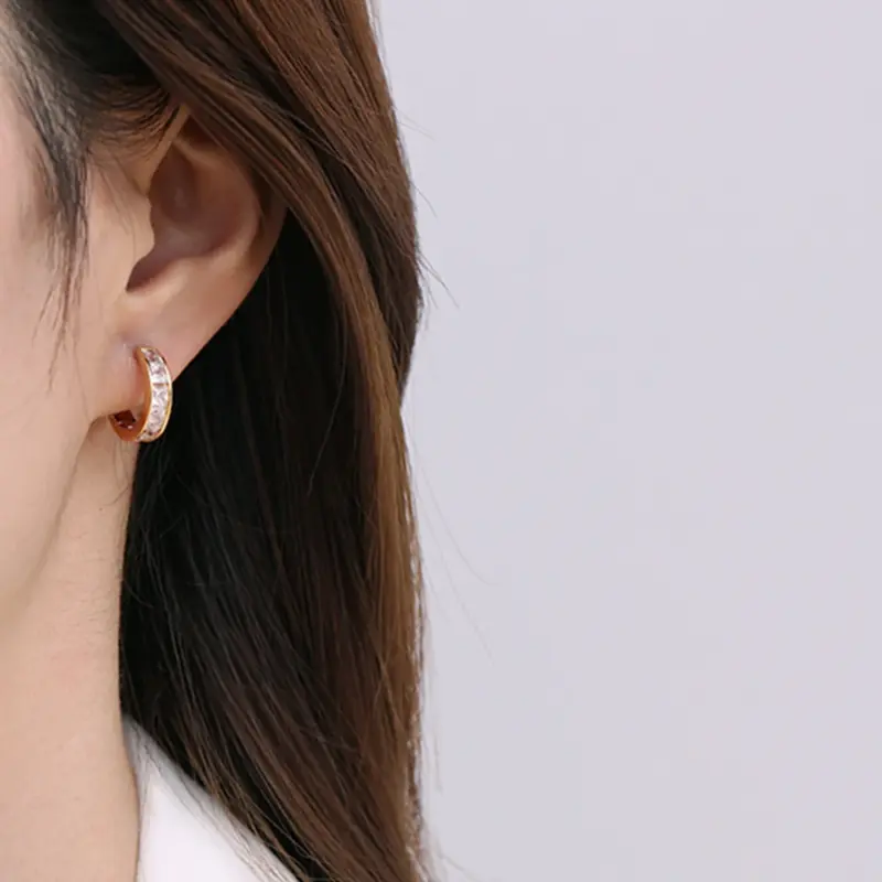 Gold ear cuff with square CZ stones on model's ear catching sunlight