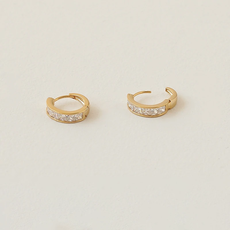 Gold ear cuff with square CZ stones on model's ear catching sunlight