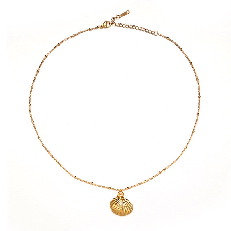 Natural tumbled shell pendant on 18K gold-plated chain styled with linen shirt and jeans at beachside café
