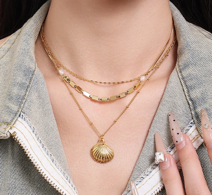 Natural tumbled shell pendant on 18K gold-plated chain styled with linen shirt and jeans at beachside café